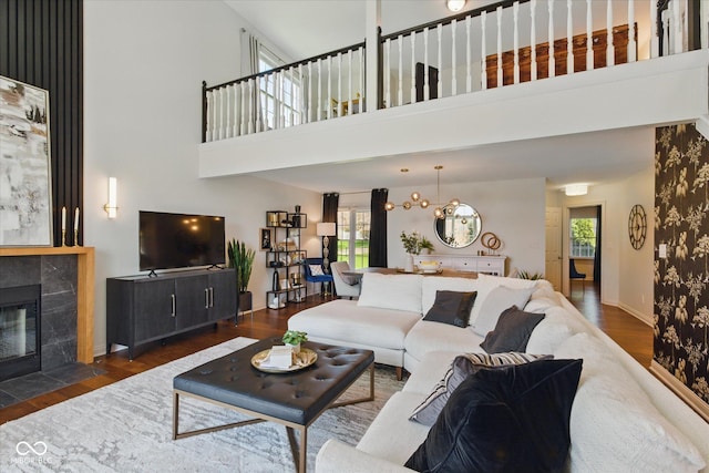 living room with a towering ceiling, plenty of natural light, wood finished floors, and a tiled fireplace
