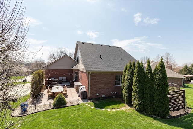 back of house with a shingled roof, brick siding, an outdoor living space, a patio area, and a lawn