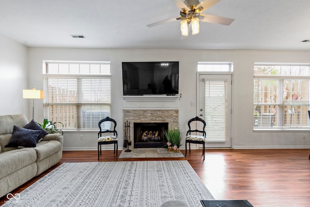 living room with wood finished floors, a fireplace, baseboards, visible vents, and a ceiling fan