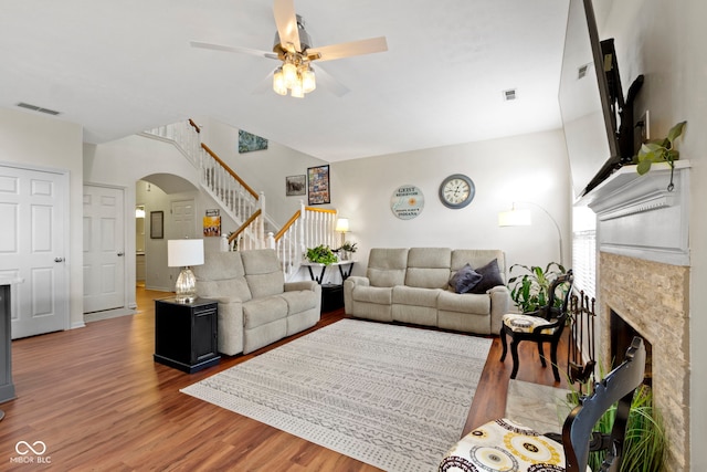 living room featuring wood finished floors, stairway, a fireplace, visible vents, and a ceiling fan