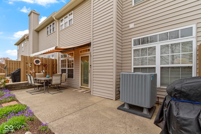 rear view of property with a chimney, a patio area, outdoor dining space, fence, and central AC unit