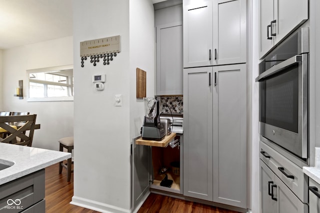 kitchen featuring baseboards, light stone countertops, oven, gray cabinetry, and dark wood-style floors