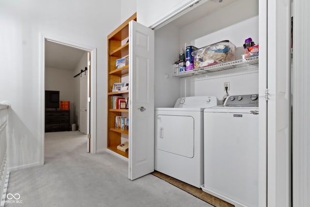 laundry room featuring a barn door, washer and dryer, light colored carpet, and laundry area