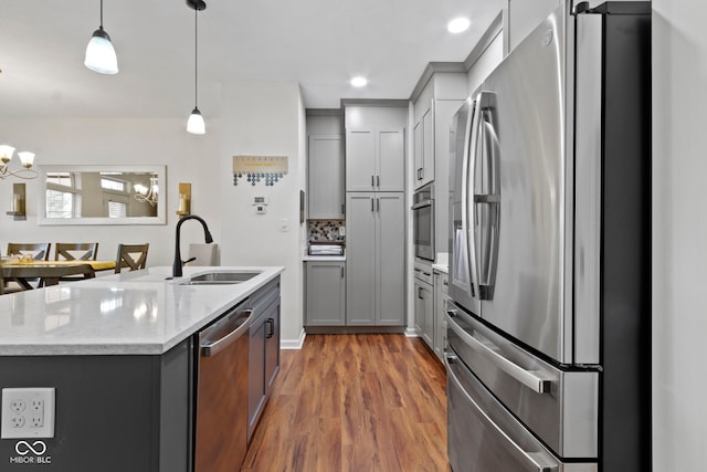 kitchen with gray cabinetry, stainless steel appliances, wood finished floors, and a sink