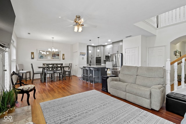living area featuring ceiling fan with notable chandelier, visible vents, baseboards, arched walkways, and dark wood finished floors