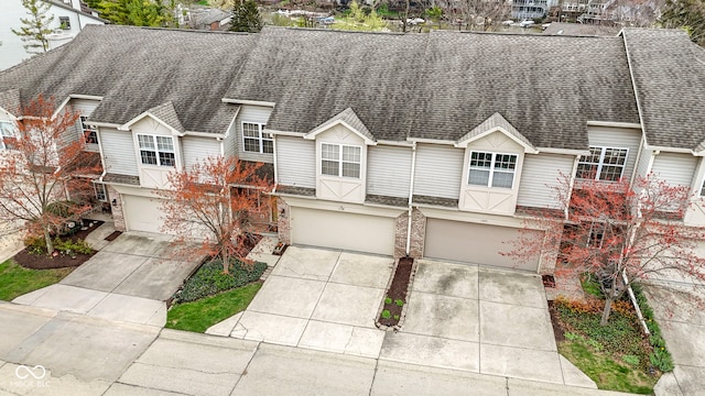 view of front facade featuring driveway, roof with shingles, stone siding, and a garage