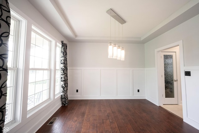 unfurnished dining area featuring a notable chandelier, a tray ceiling, visible vents, and dark wood-type flooring