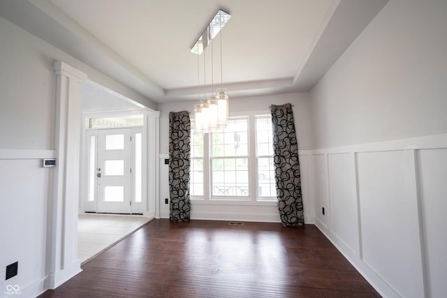 unfurnished dining area featuring visible vents, a decorative wall, a wainscoted wall, wood-type flooring, and a tray ceiling