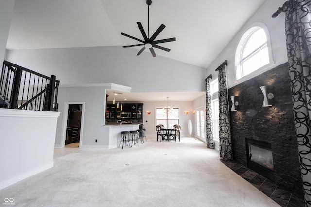 living room featuring a healthy amount of sunlight, a fireplace, high vaulted ceiling, carpet, and ceiling fan with notable chandelier