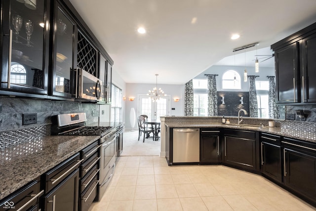 kitchen with a notable chandelier, a sink, dark cabinetry, stainless steel appliances, and tasteful backsplash