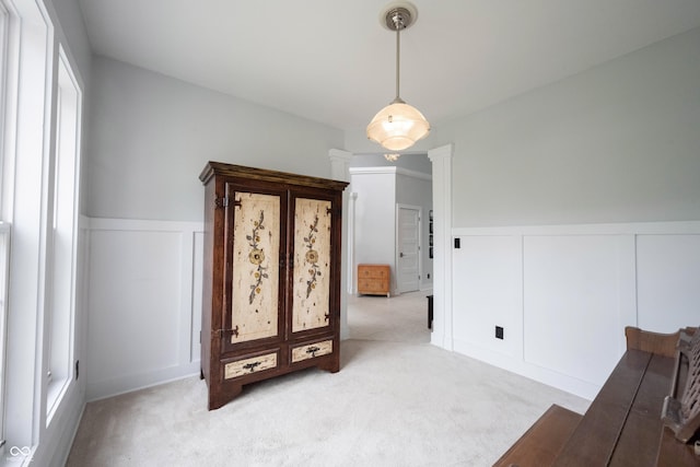 interior space featuring ornate columns, light carpet, a wainscoted wall, and a decorative wall