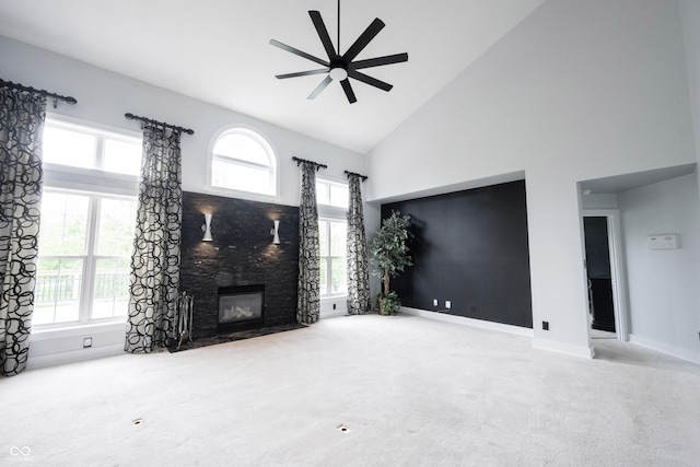 unfurnished living room with ceiling fan, a fireplace with flush hearth, high vaulted ceiling, carpet floors, and a wealth of natural light