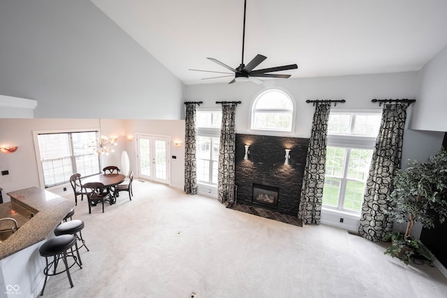 carpeted living area with ceiling fan, a stone fireplace, a healthy amount of sunlight, and high vaulted ceiling
