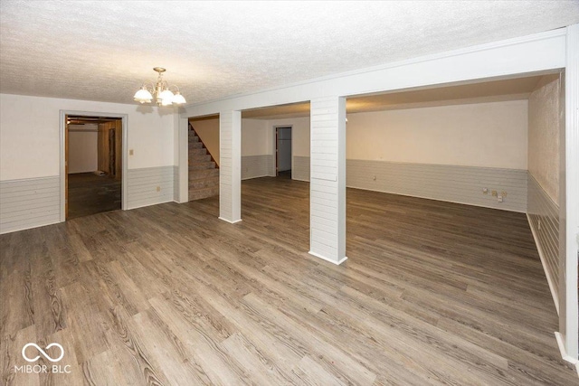below grade area featuring an inviting chandelier, a textured ceiling, wood finished floors, and wainscoting