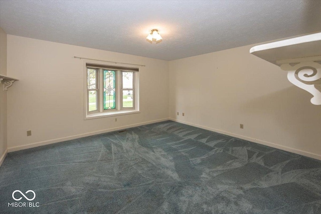spare room with dark colored carpet, a textured ceiling, and baseboards