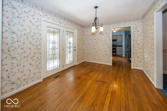 unfurnished dining area with hardwood / wood-style floors, wallpapered walls, a chandelier, and visible vents