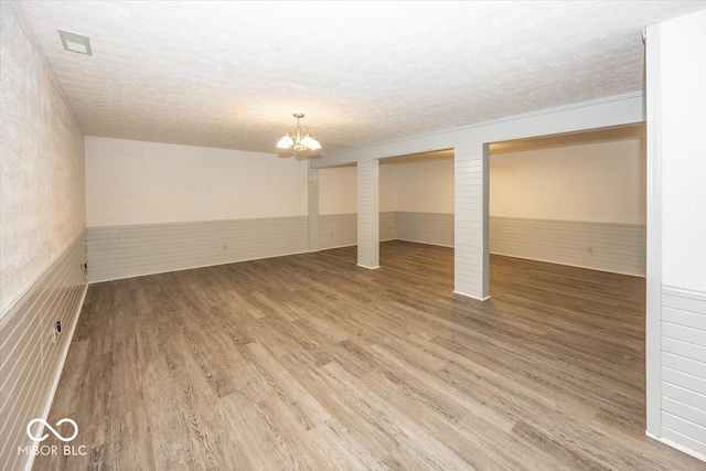 basement with a textured ceiling, wood finished floors, and wainscoting