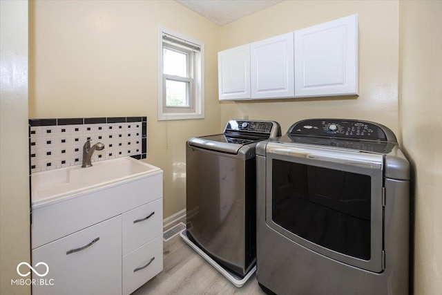 washroom with cabinet space, washing machine and clothes dryer, a sink, baseboards, and light wood-type flooring