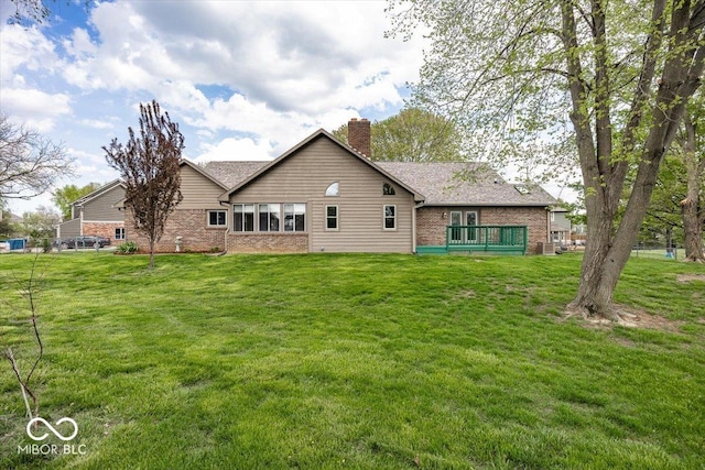 rear view of house featuring a chimney, brick siding, a deck, and a yard