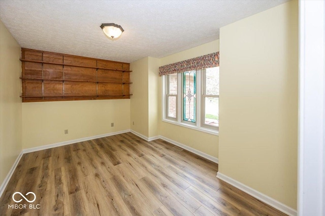 empty room featuring a textured ceiling, light wood-style flooring, and baseboards