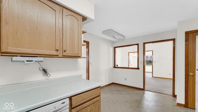 kitchen featuring light countertops, baseboards, light brown cabinetry, and white dishwasher