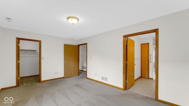 unfurnished bedroom with a walk in closet, visible vents, baseboards, and carpet floors