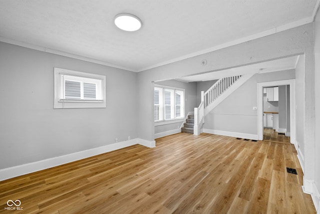 unfurnished living room with visible vents, baseboards, stairway, and light wood-style floors