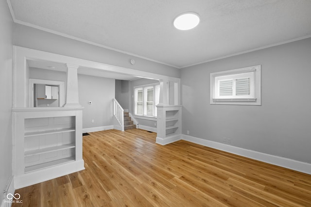 empty room featuring ornamental molding, baseboards, light wood finished floors, and stairs