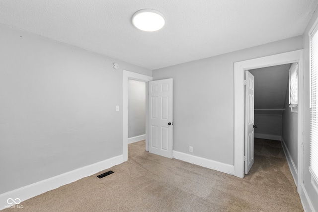 unfurnished bedroom featuring baseboards, a spacious closet, carpet flooring, a textured ceiling, and visible vents
