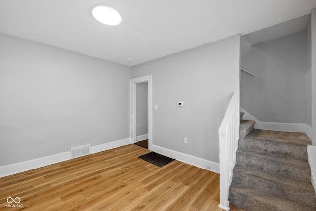 unfurnished room featuring visible vents, baseboards, light wood-type flooring, and stairway