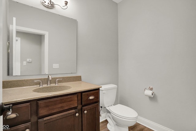 half bath with toilet, baseboards, wood finished floors, and vanity