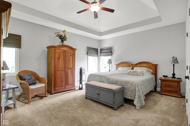 bedroom with ceiling fan, light colored carpet, and a raised ceiling