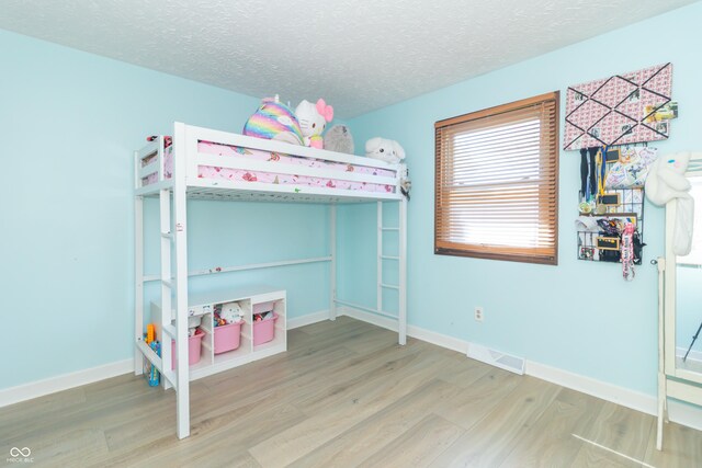 bedroom featuring visible vents, a textured ceiling, baseboards, and wood finished floors