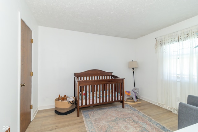 bedroom with a textured ceiling, wood finished floors, and a crib