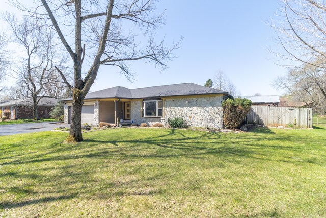 view of front of property with a front yard, an attached garage, stone siding, fence, and driveway