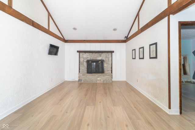 unfurnished living room with a stone fireplace, baseboards, wood finished floors, and lofted ceiling
