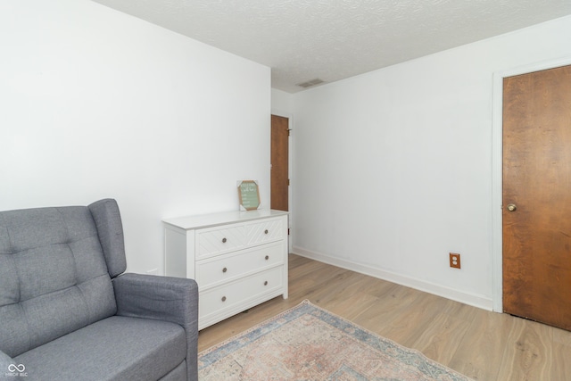living area with baseboards, visible vents, light wood-type flooring, and a textured ceiling
