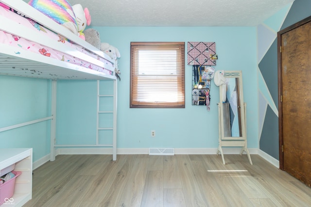 unfurnished bedroom with a textured ceiling, wood finished floors, baseboards, and visible vents