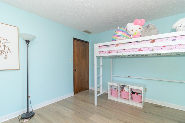 bedroom with a textured ceiling, wood finished floors, baseboards, and visible vents