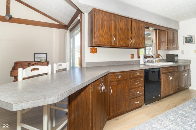 kitchen featuring black dishwasher, a sink, a textured ceiling, vaulted ceiling, and light wood-style flooring