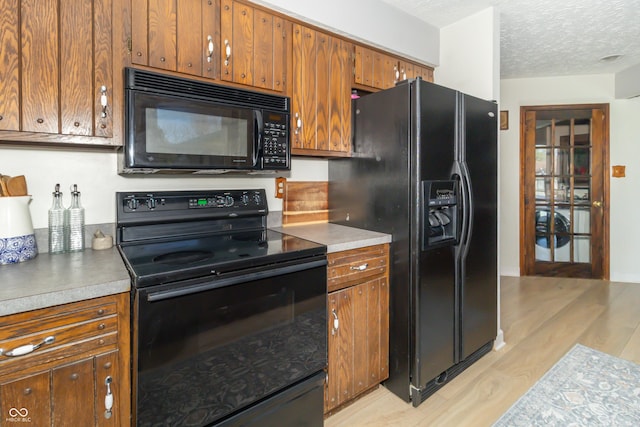 kitchen with brown cabinetry, a textured ceiling, black appliances, and light wood-style flooring