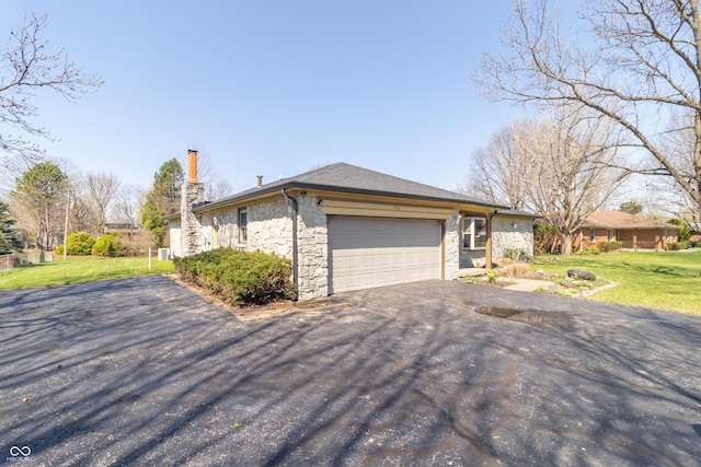 view of home's exterior with an attached garage, stone siding, a lawn, a chimney, and aphalt driveway