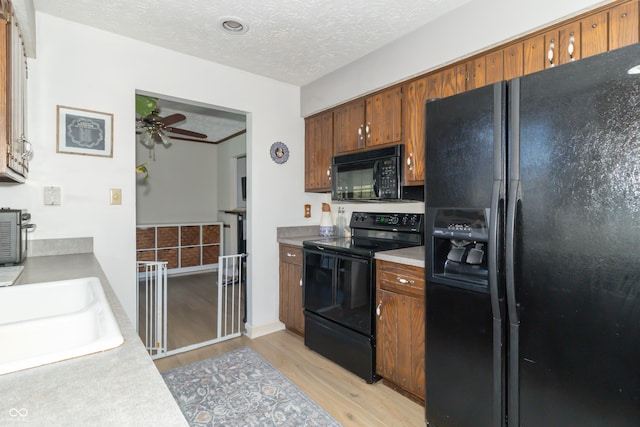 kitchen featuring a sink, light wood-type flooring, a ceiling fan, a textured ceiling, and black appliances