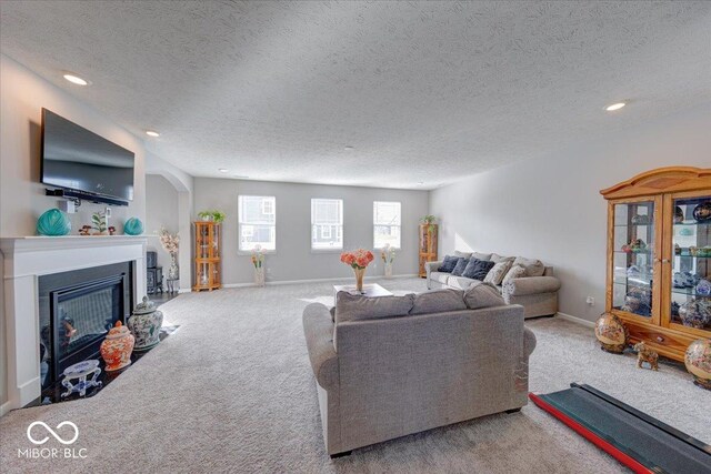 5839 Altar Bell Cir, Greenwood, IN 46143 - carpeted living area with arched walkways, a textured ceiling, a glass covered fireplace, recessed lighting, and baseboards