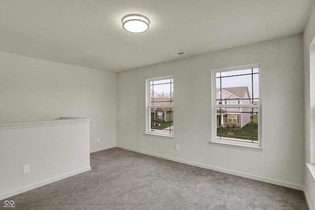 carpeted empty room with a healthy amount of sunlight, baseboards, and visible vents