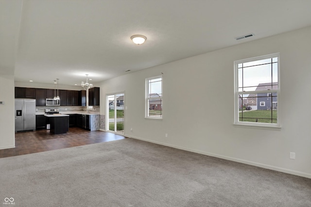 unfurnished living room with visible vents, baseboards, dark colored carpet, and an inviting chandelier