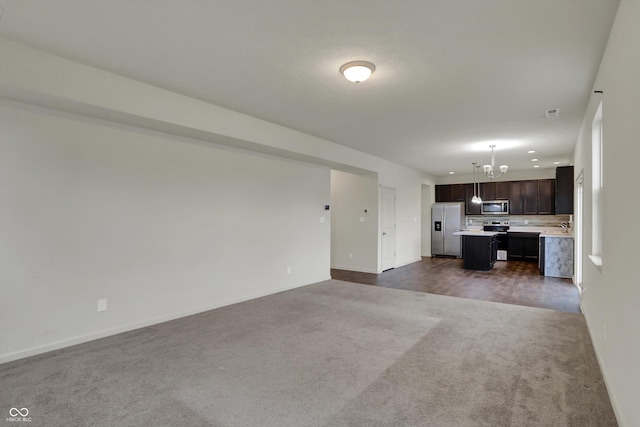 unfurnished living room with baseboards, dark colored carpet, and an inviting chandelier