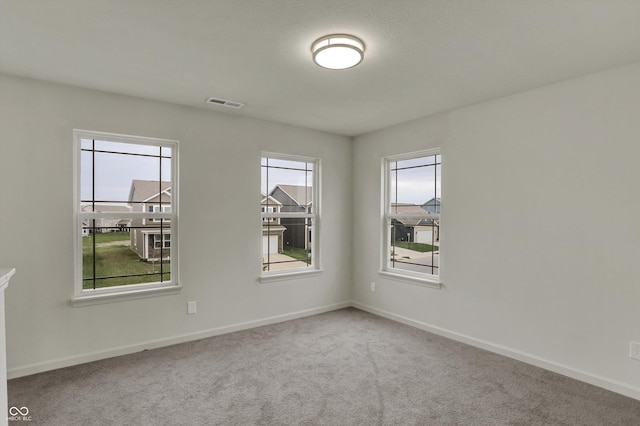 empty room with carpet flooring, visible vents, and a healthy amount of sunlight