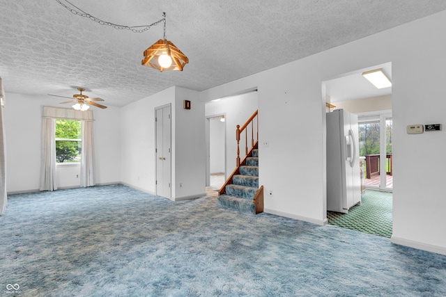 unfurnished living room featuring a healthy amount of sunlight, carpet flooring, stairs, and a textured ceiling