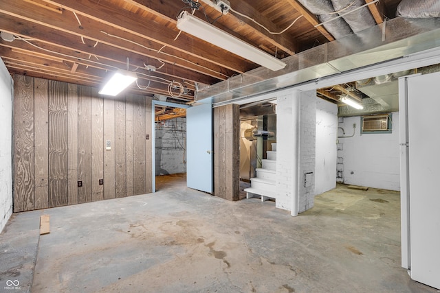 unfinished basement featuring a wall mounted air conditioner, freestanding refrigerator, stairs, and wooden walls